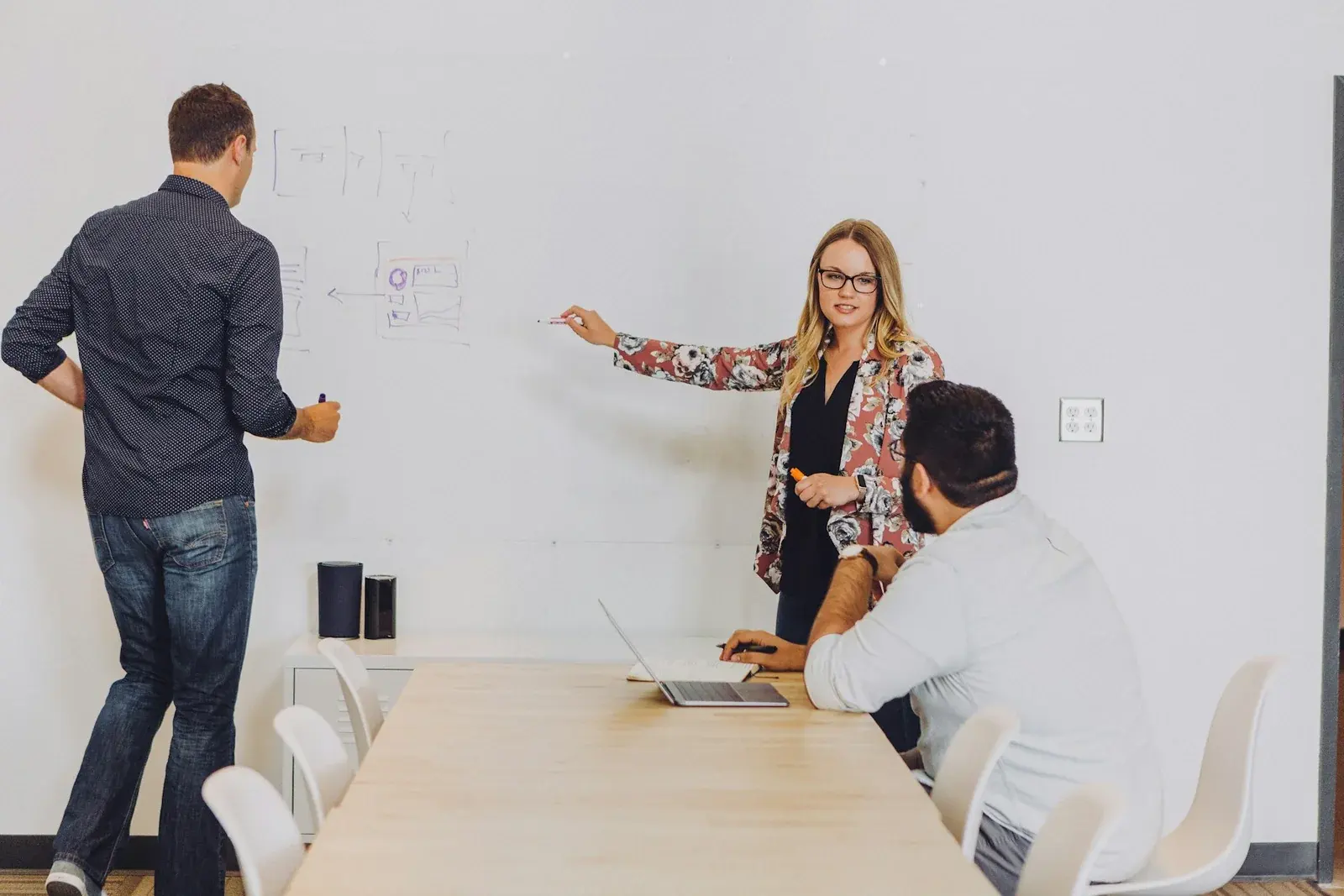 Three people discussing interface sketches on a whiteboard beside a laptop