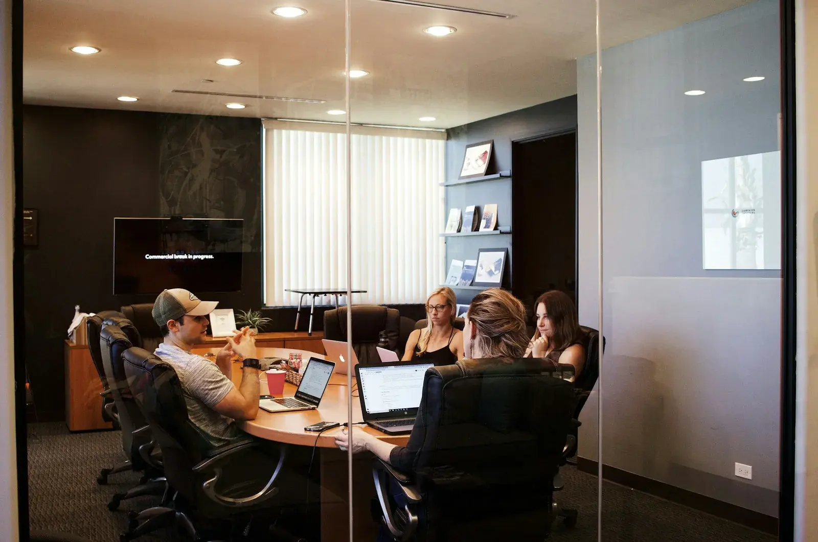 Four colleagues meeting around laptops in a glass-walled conference room
