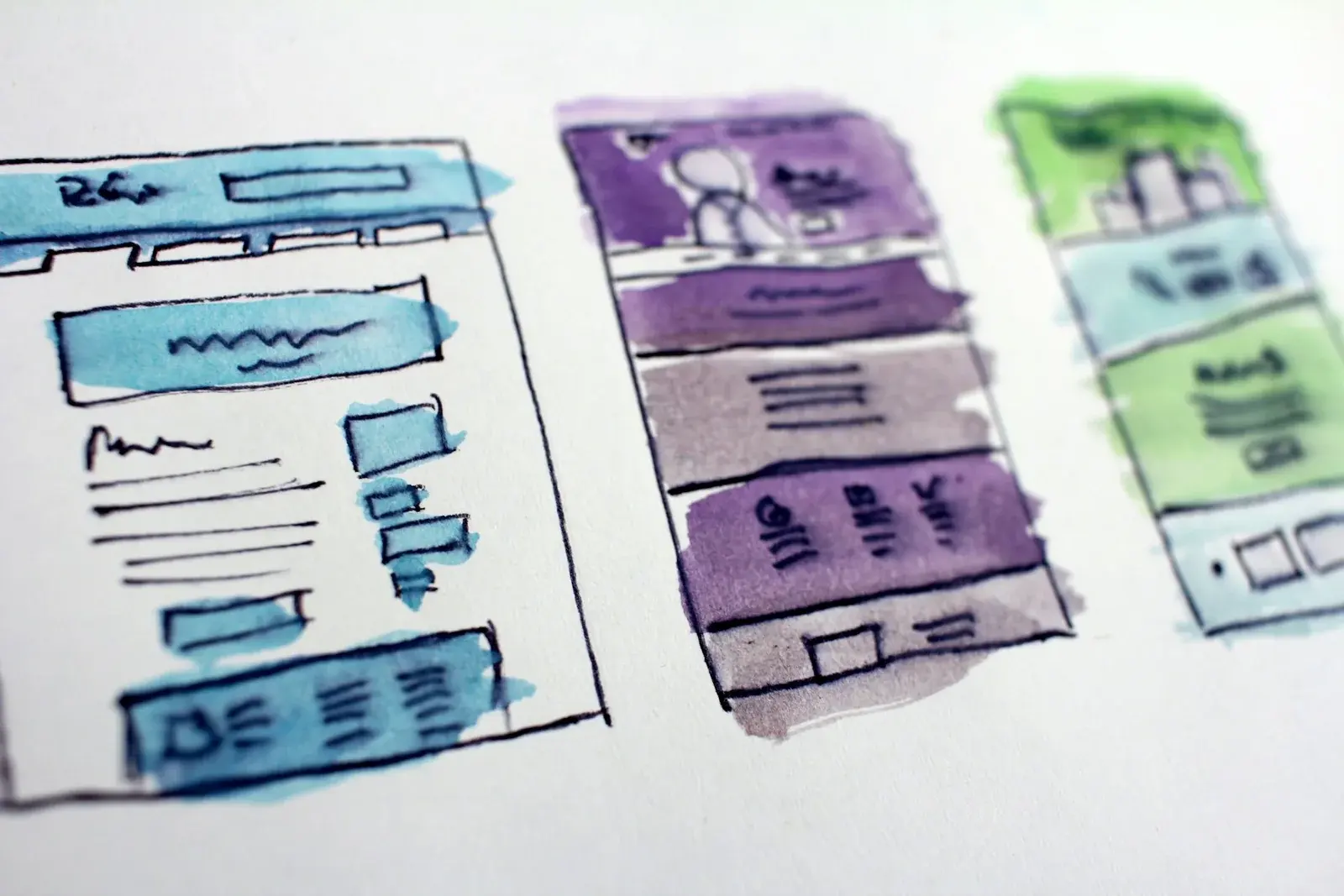 Watercolor wireframe sketches of three website layouts on paper